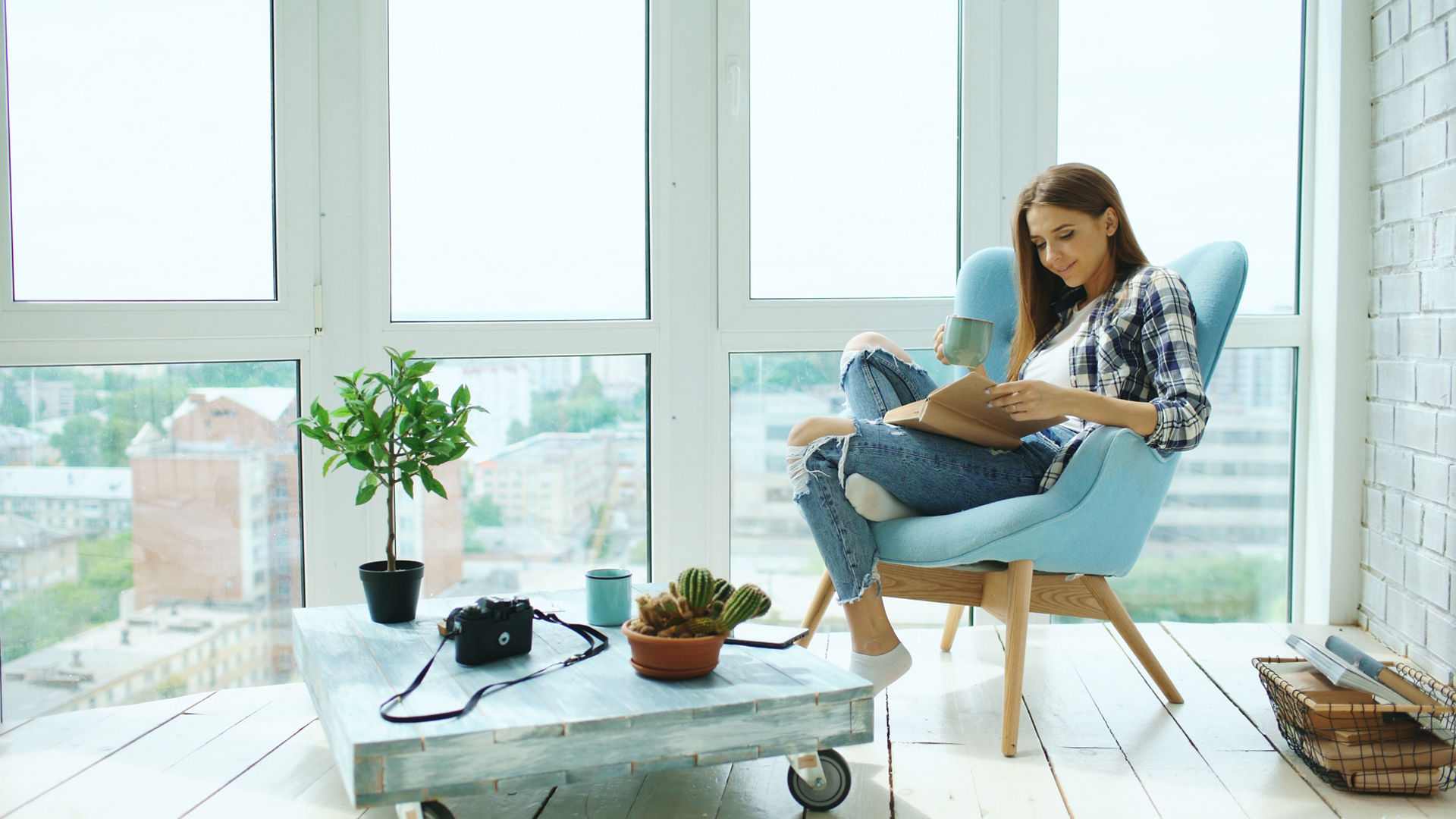 Young attractive woman read book and drink coffee sitting on balcony in modern loft apartment