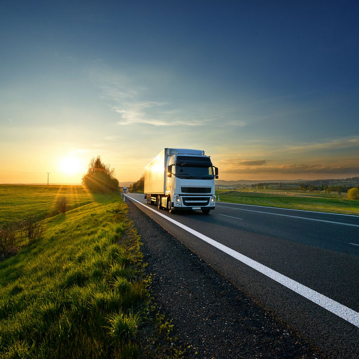 White truck driving on the asphalt road in rural landscape at sunset; Shutterstock ID 720072589