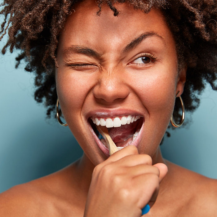 Close up shot of happy joyful funny dark skinned young woman has Afro hair brushes teeth actively with toothbrush, opens mouth broadly, blinks eye, shows bare shoulders, cares of oral hygiene; Shutterstock ID 1335284804; purchase_order: COG PC Oral Care Brochure; job: Oral Care Brochure; client: Omya; other: Phana Tuon
1335284804