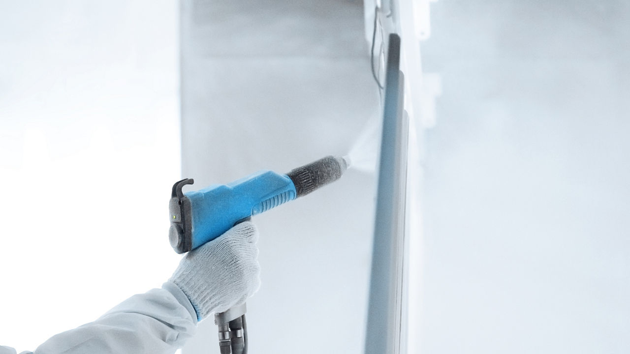 Hand of a worker in a protective work wear holding powder coating sprayer in a metal producing factory