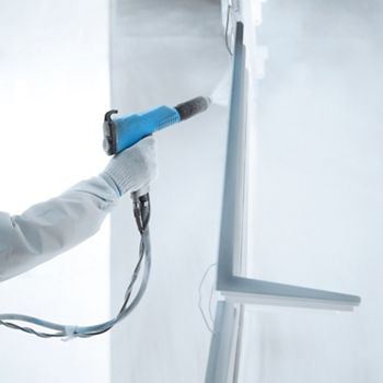 Hand of a worker in a protective work wear holding powder coating sprayer in a metal producing factory