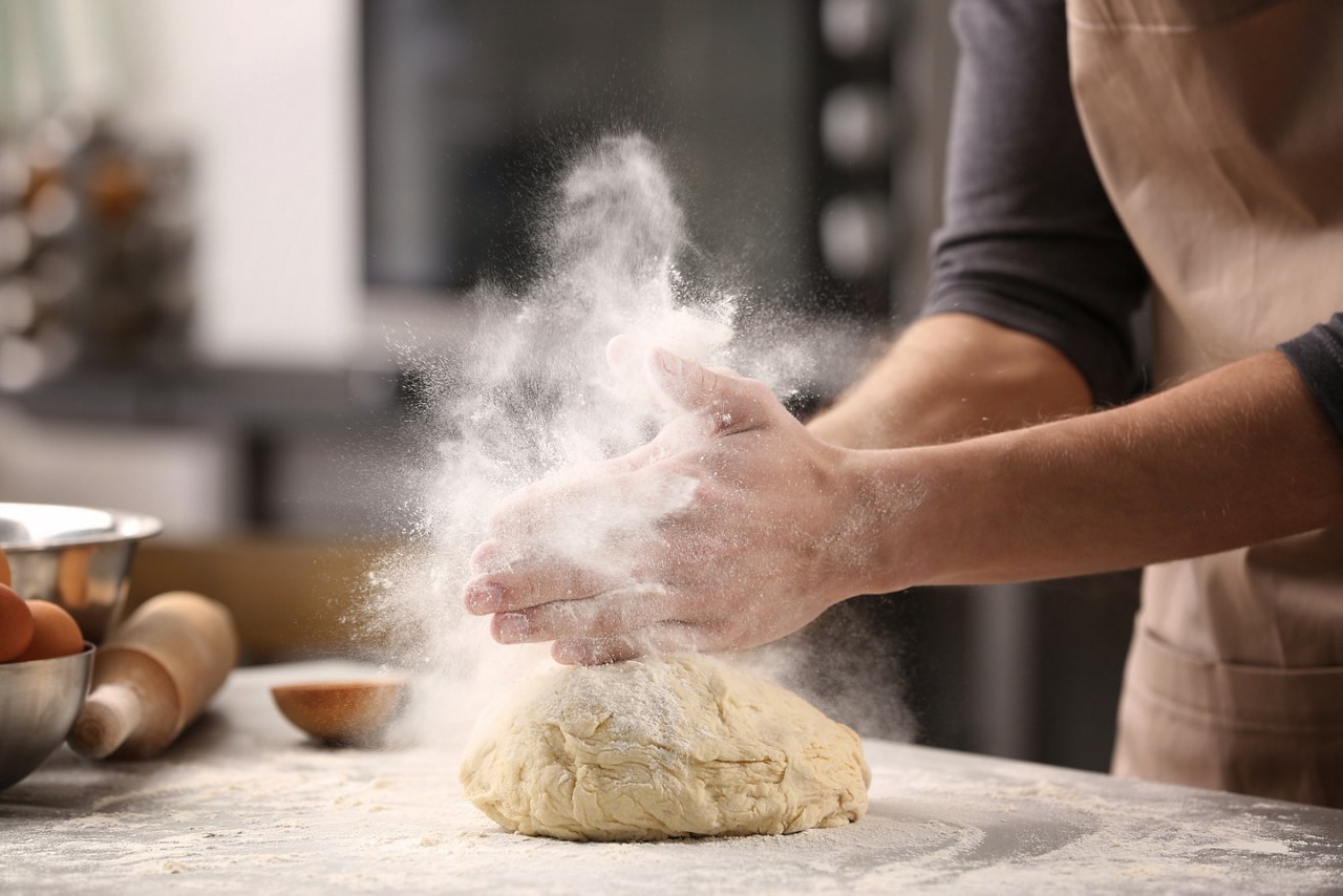 Male hands clapping and sprinkling white flour over dough on kitchen background; Shutterstock ID 576353752