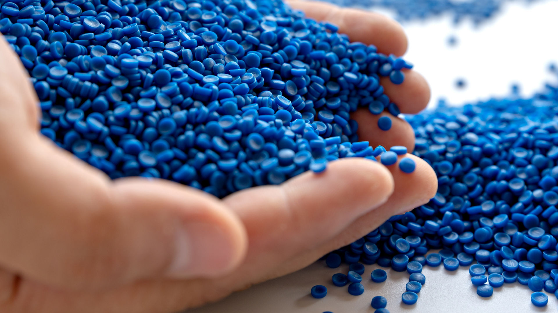 Omya Polymer Product Solutions - hands cupping blue masterbatch pellets 