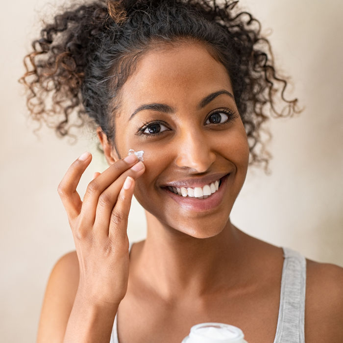 Smiling african girl with applying facial moisturizer while holding jar and looking at camera. Portrait of young black woman applying cream on her face isolated on beige background with copy space.; Shutterstock ID 1593933484; purchase_order: COG; job: COG; client: COG; other: COG
1593933484