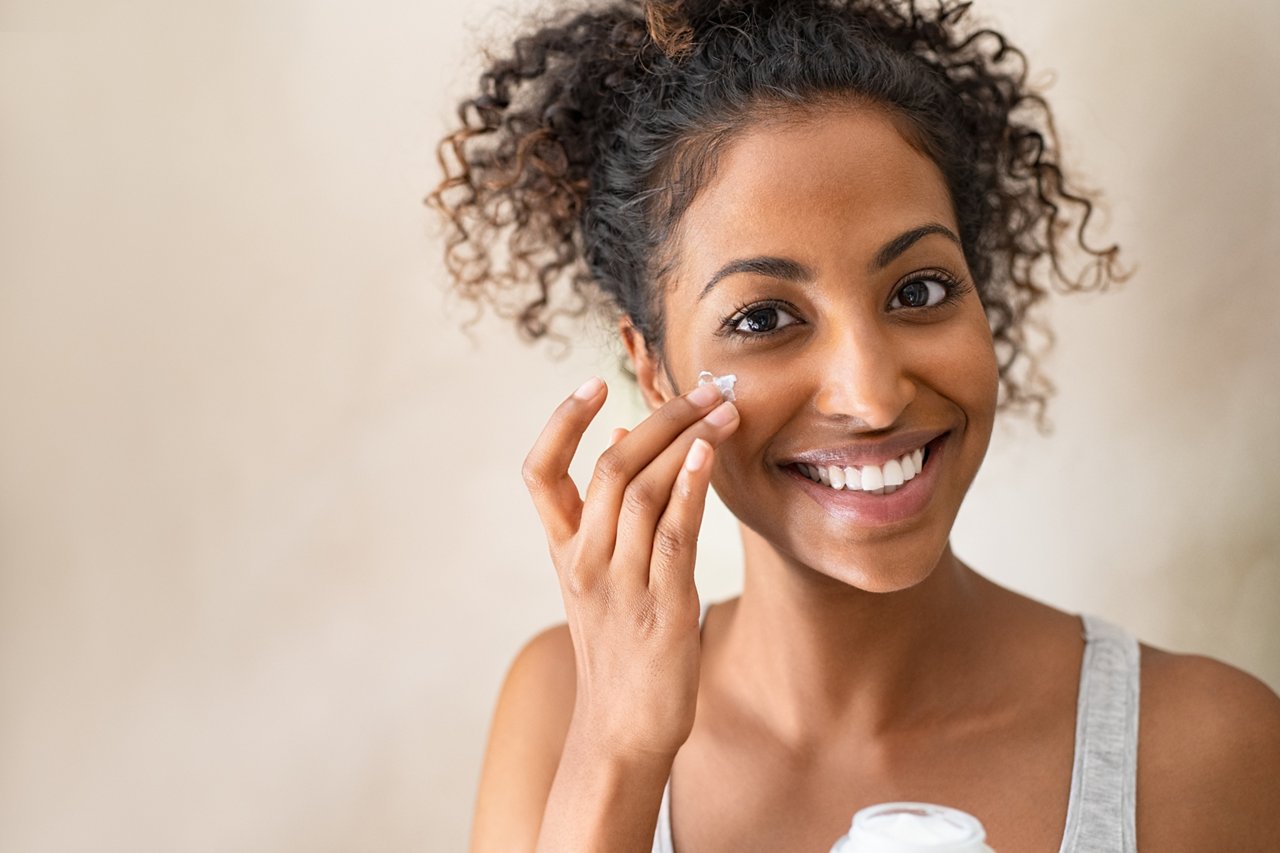 Smiling african girl with applying facial moisturizer while holding jar and looking at camera. Portrait of young black woman applying cream on her face isolated on beige background with copy space.; Shutterstock ID 1593933484; purchase_order: COG; job: COG; client: COG; other: COG
1593933484