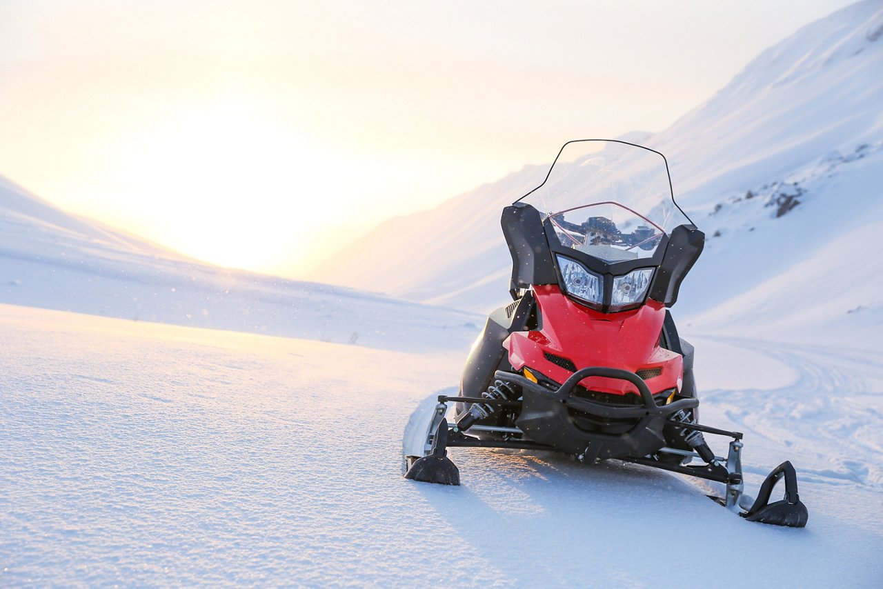 red snowmobile on a background of snowy mountains on a sunny day.