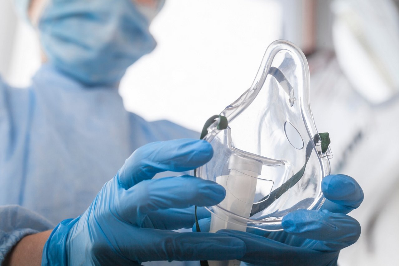doctor in protective equipment and gloves put on oxygen mask patient diagnosis of coronavirus and Pneumonia  ; Shutterstock ID 1695703903; purchase_order: OPP Media & Collateral; job: ; client: ; other: 