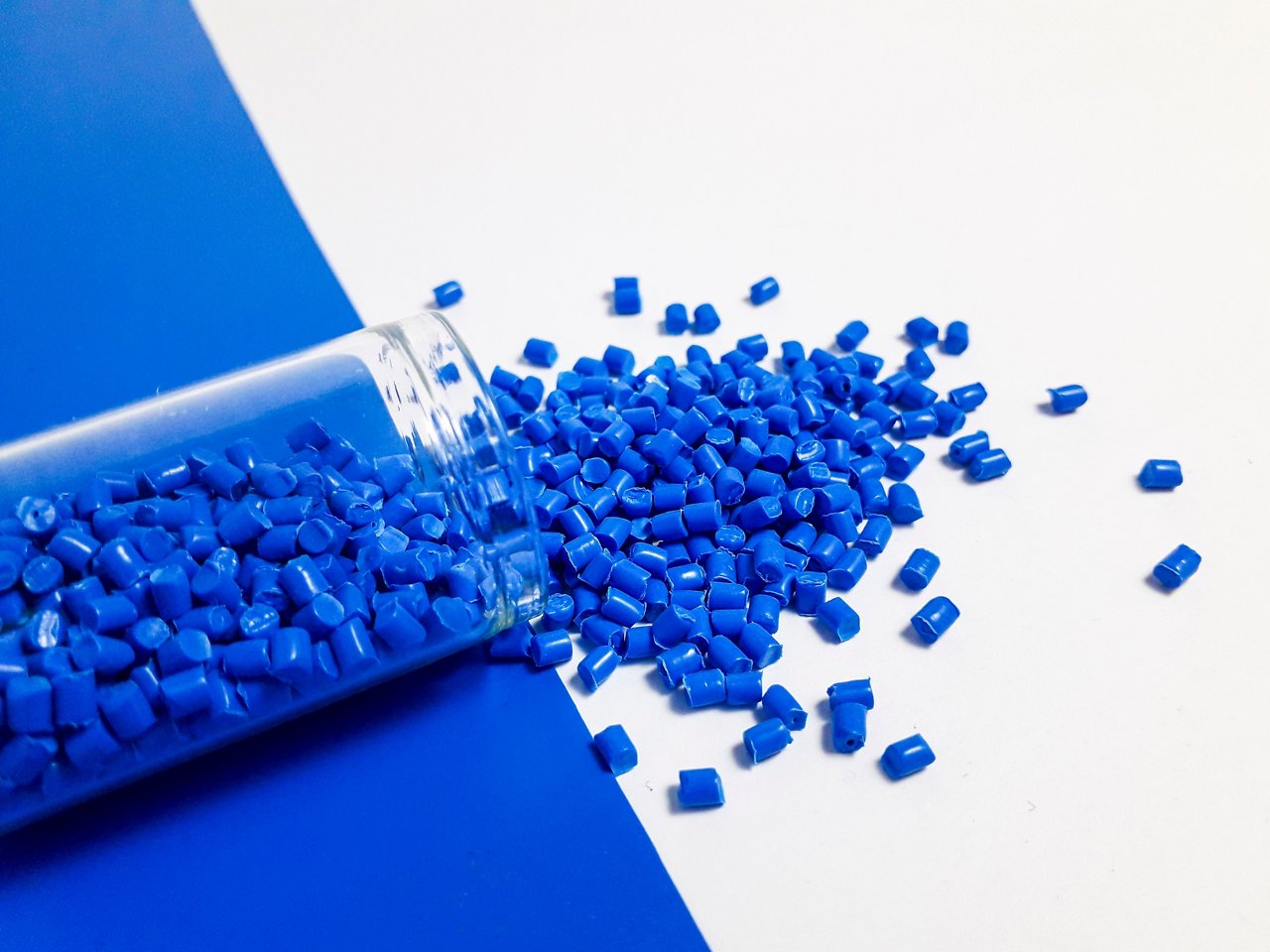 Blue masterbatch granules with glass tube on white and blue background,color pigment carrier polymer in plastic industry,suitable for plastic company catalogue; Shutterstock ID 2552721619; purchase_order: CORP; job: Turkey Landing Page; client: ; other: 