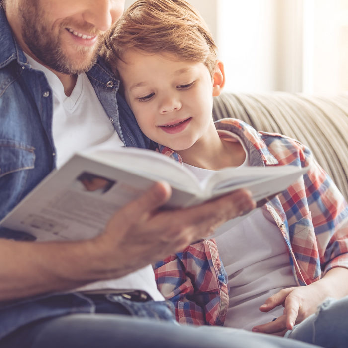 Father and son reading a book and smiling while spending time together at home