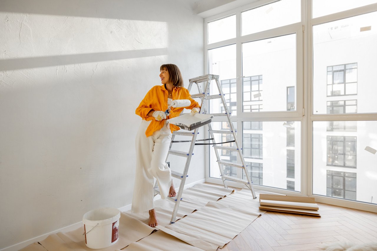 Portrait of a young woman making repairing in apartment, standing with paint roller near ladder in bright room of her new home; Shutterstock ID 2202224669; purchase_order: CON; job: ; client: ; other:2202224669